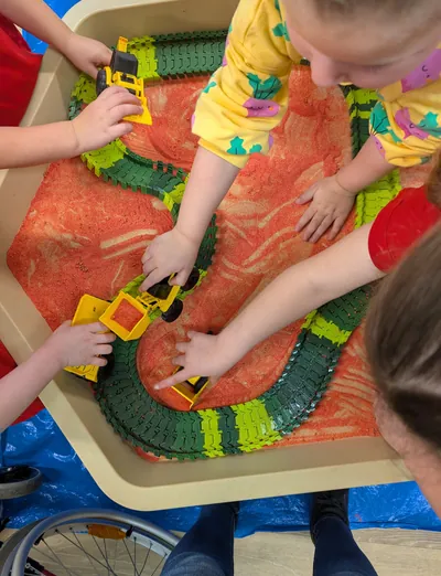 Children's hands playing with toy diggers in a sensory tray at Lakeside Creative Minds